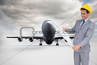 Composite image of smiling architect with hard hat looking at plans