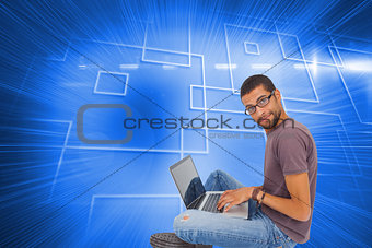 Composite image of man wearing glasses sitting on floor using laptop and looking at camera
