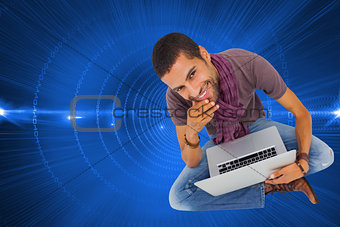 Composite image of thoughtful man sitting on floor using laptop and smiling at camera