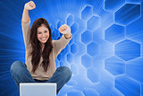 Composite image of woman looks straight ahead as she celebrates in front of her laptop