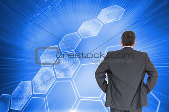 Composite image of businessman standing back to the camera with hands on hip