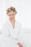 Woman in bathrobe and hair curlers sitting on bed