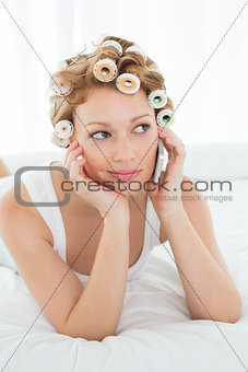 Woman in hair curlers using cellphone while lying in bed