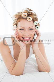 Woman in hair curlers using cellphone while lying in bed