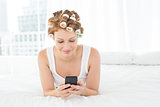 Woman in hair curlers text messaging while lying in bed