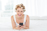 Cheerful woman in hair curlers text messaging in bed