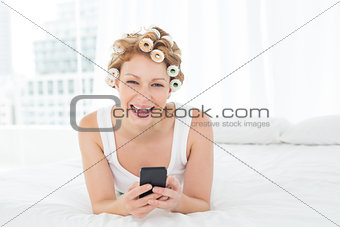 Cheerful woman in hair curlers text messaging in bed