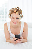 Woman in hair curlers text messaging in bed