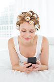 Relaxed woman in hair curlers text messaging in bed