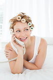 Beautiful woman in hair curlers using phone in bed