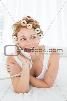 Beautiful woman in hair curlers using phone in bed