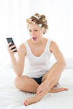 Shocked woman in hair curlers reading text message on bed