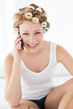 Woman in hair curlers using cellphone on bed
