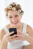Woman in hair curlers text messaging on bed