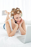 Woman in hair curlers using cellphone and laptop in bed