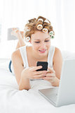 Woman in hair curlers text messaging by laptop in bed