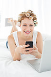 Woman in hair curlers text messaging by laptop in bed