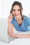 Smiling woman using mobile phone and laptop in bed