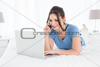 Woman using mobile phone and laptop in bed