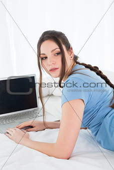 Woman using laptop as she looks away in bed