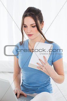 Woman using laptop as she holds a notepad on bed