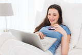 Cheerful casual woman doing online shopping in bed