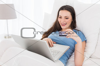 Cheerful casual woman doing online shopping in bed