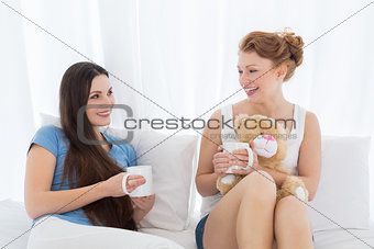 Cheerful female friends with coffee cups in bed