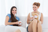 Cheerful young female friends with coffee cups in bed