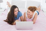Relaxed young female friends using laptop in bed