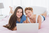 Portrait of happy relaxed friends using laptop in bed