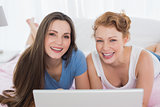 Relaxed female friends using laptop in bed