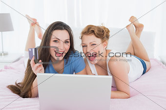 Cheerful female friends  doing online shopping in bed