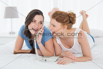 Happy woman with friend using phone in bed