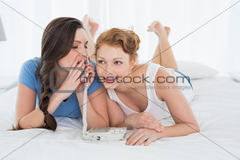 Woman with friend using phone while lying in bed