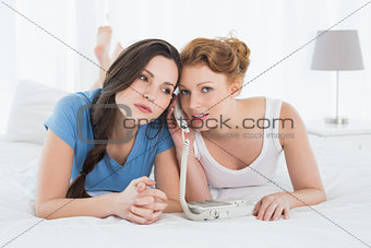 Beautiful woman with friend using phone in bed