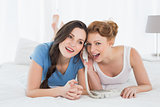Cheerful woman with friend using phone in bed