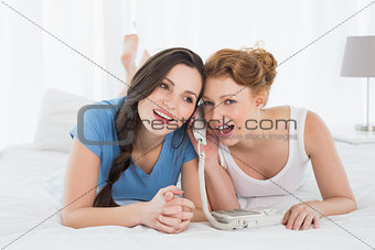 Cheerful woman with friend using phone in bed