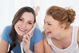 Woman with cheerful friend using phone in bed