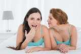 Female friends in tank tops gossiping in bed