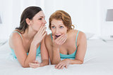 Female friends in tank tops gossiping in bed