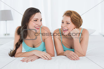 Cheerful female friends in teal tank tops lying in bed