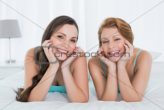 Happy female friends in teal tank tops lying in bed