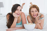 Cheerful friends with remote control and popcorn in bed