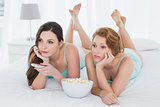 Female friends with remote control and popcorn in bed