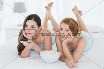 Female friends with remote control and popcorn in bed