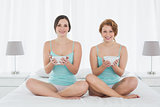 Smiling female friends with salad bowls sitting on bed