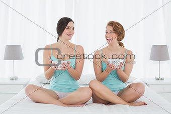 Female friends with salad bowls sitting on bed