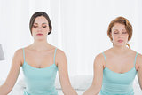Women with eyes closed sitting in meditation posture on bed