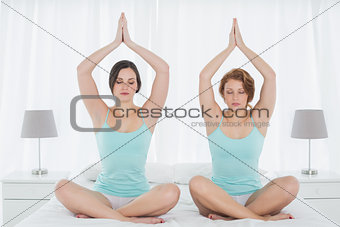 Two women sitting with joined hands over head in bedroom